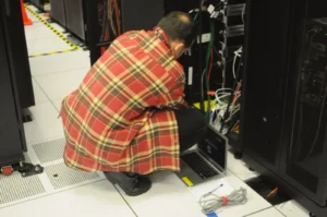 Technicien travaillant sur une baie de serveurs en salle informatique, photo d'illustration